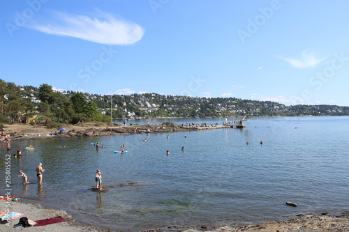 Oslo, Norway - July 22, 2018: Beach in Oslo Fjord. Beach is located on Ulvoya island of the inner Oslofjord, just east of the city center. People relax sunbathing and swimming on beach on hot summer d photo