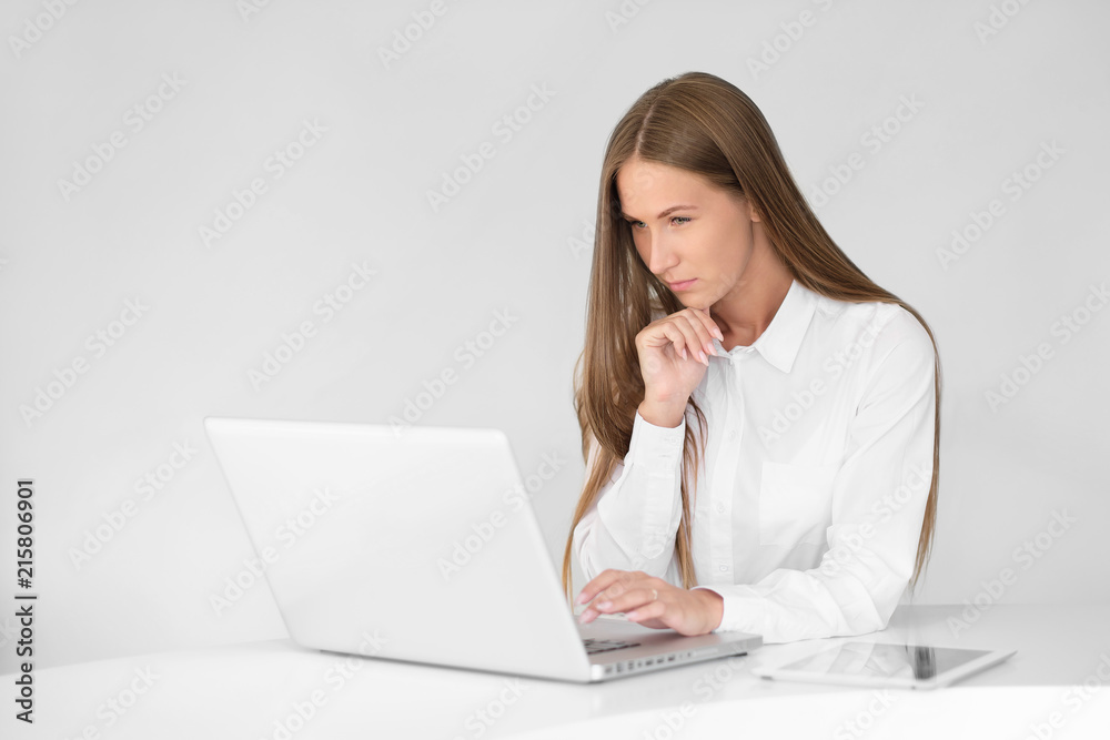 Young beautiful woman is working on a laptop in the office on a white background. Young beautiful woman is working on a laptop in the office on a white background.