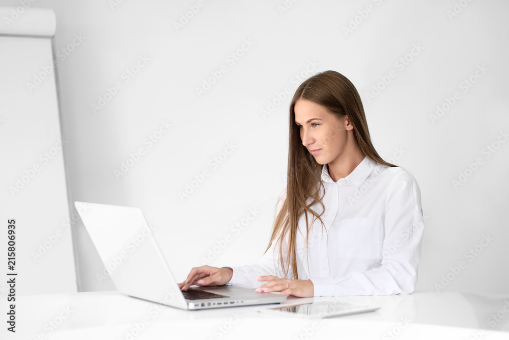 Young beautiful woman is working on a laptop in the office on a white background. Young beautiful woman is working on a laptop in the office on a white background.