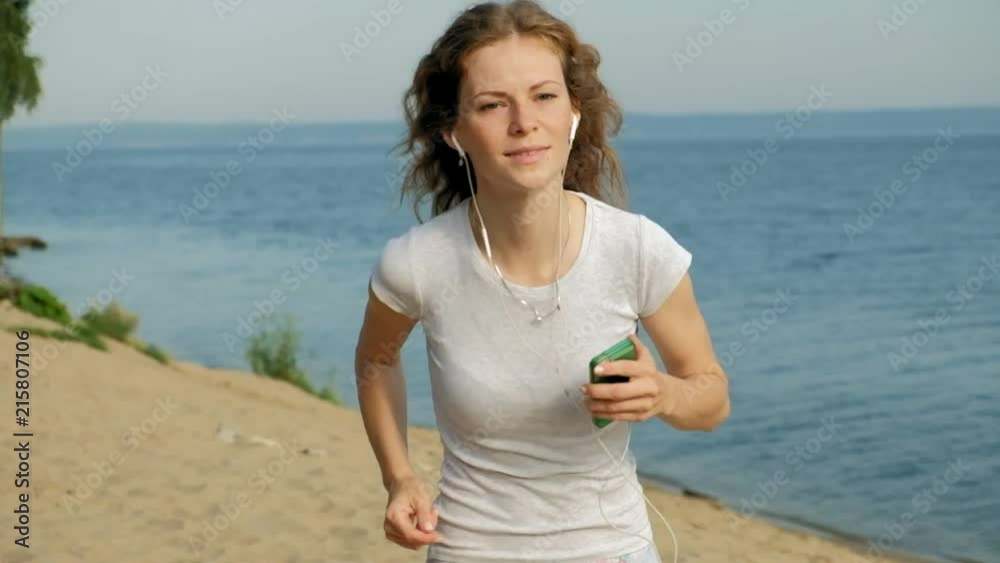 A young woman with a fine figure is engaged in gymnastics in the sea at dawn. She runs along the seacoast in headphones, Super slow motion A young woman with a fine figure is engaged in gymnastics in the sea at dawn. She runs along the seacoast in headphones, Super slow motion