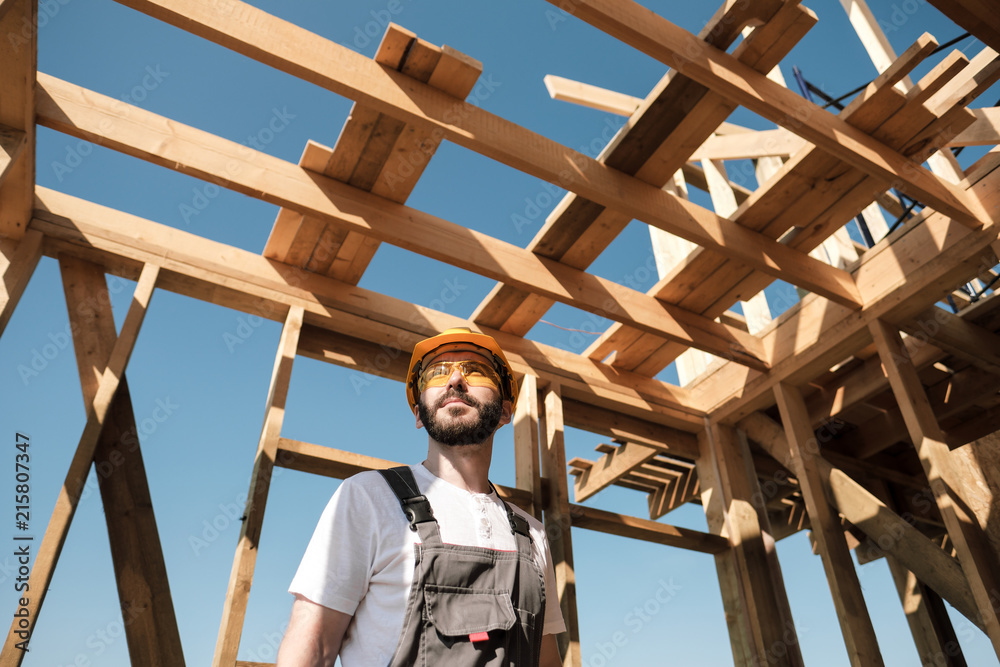 The man is a builder on the roof of a wooden frame house. The man is a builder on the roof of a wooden frame house.