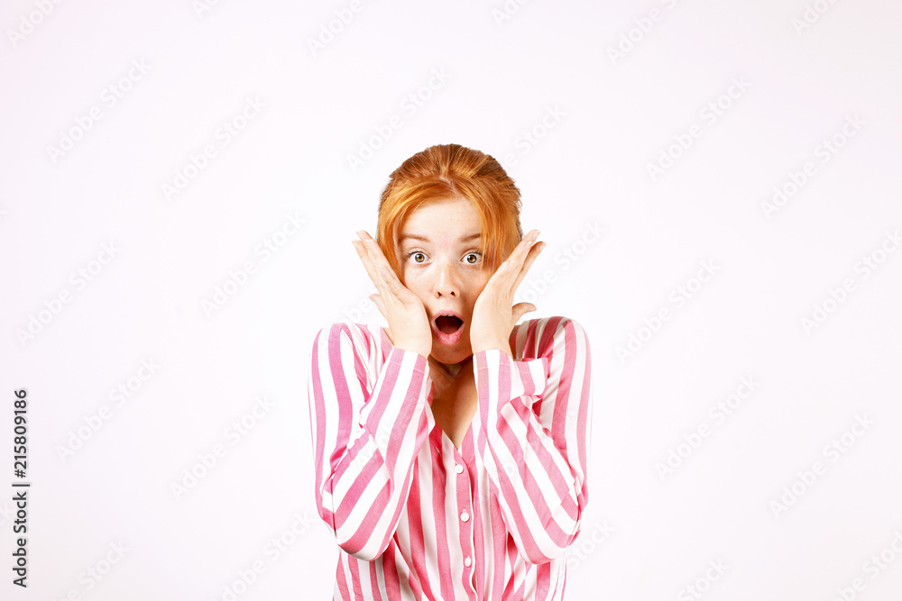 Beautiful redhead young woman looking scared, eyes wide open, hands on face. Pretty female with childish frightened facial expression, reaction to scary movie. White background, copy space, close up. Beautiful redhead young woman looking scared, eyes wide open, hands on face. Pretty female with childish frightened facial expression, reaction to scary movie. White background, copy space, close up.