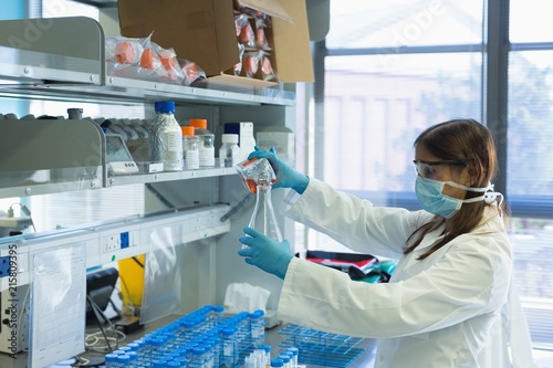 Scientist pouring chemical solution on conical flask from bottle