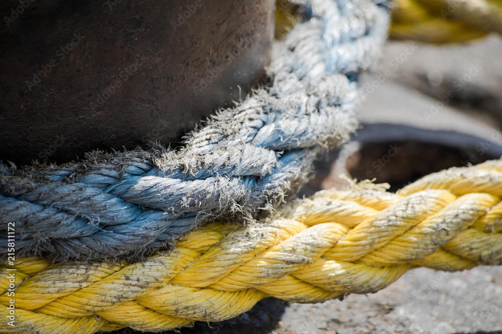 Fototapeta premium Yellow and blue thick sea ropes tied around bitt