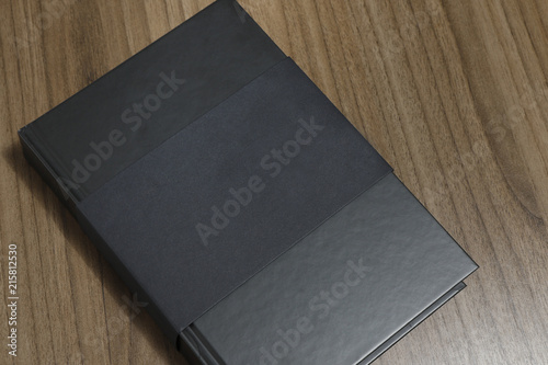 Black hardcover book with protector on wooden surface - mock-up black book