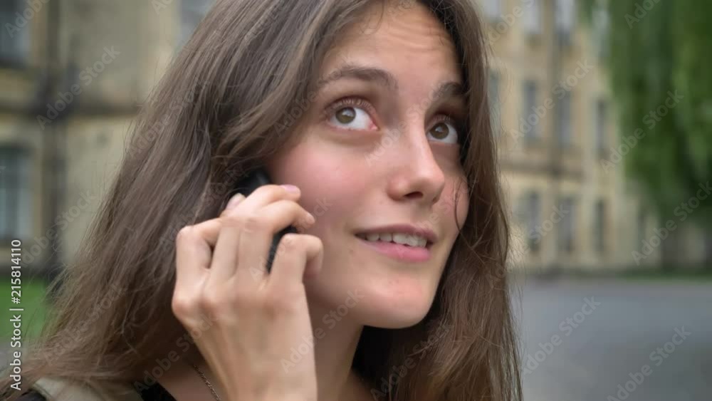 Portrait of young beautiful woman with long hair talking on phone and laughing, standing in park near university, student concept Portrait of young beautiful woman with long hair talking on phone and laughing, standing in park near university, student concept
