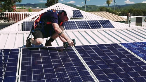 Solar panel technician with drill installing solar panels on roof on a sunny day