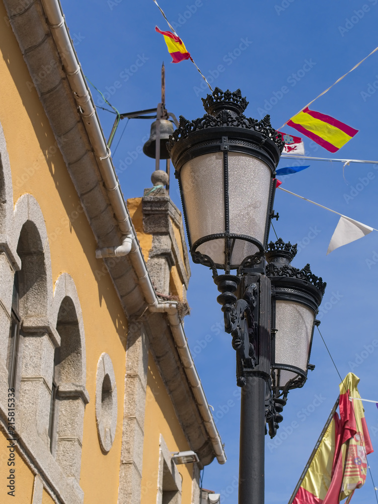 Close-up of traditional cast iron street lamps. Beautiful building with bell tower, hanging bunting and blue sky in the background at a village in Spain.