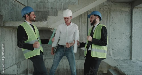 Three architects dancing in the construction site at the end of working day , wearing a high visibility vests and hard hats. photo