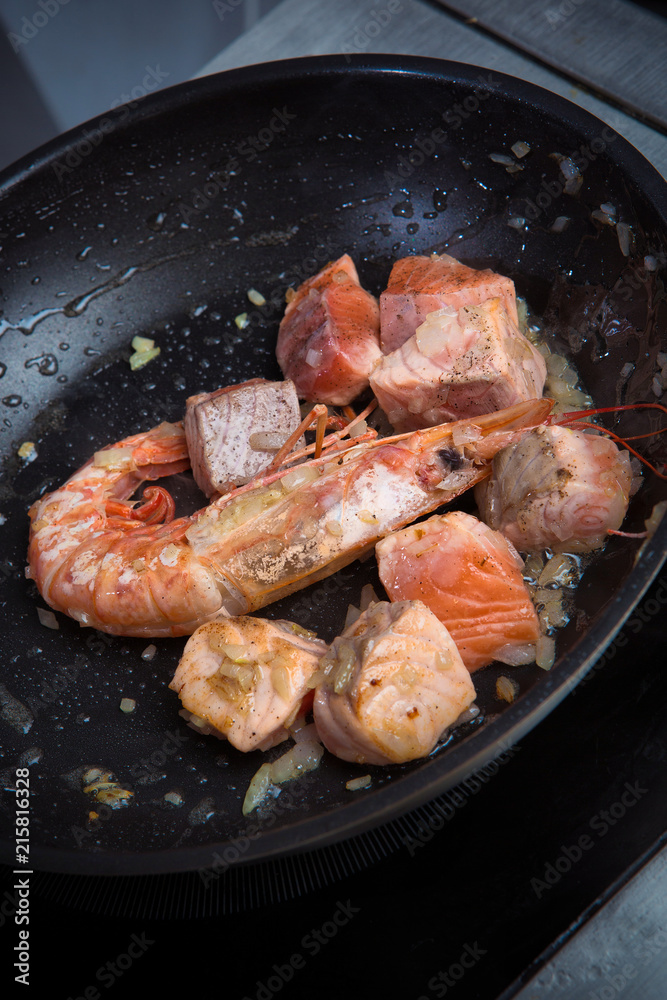 pieces of salmon and shrimp are fried in oil in a frying pan pieces of salmon and shrimp are fried in oil in a frying pan