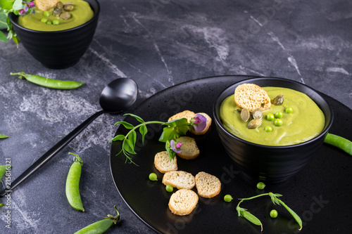 Green pea soup puree with croutons in black bowl. On dark stone background