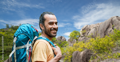 adventure, travel, tourism, hike and people concept - smiling man with backpack over background of seychelles island
