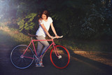 Young pretty romantic girl walking with bicycle on the sunset in green summer park