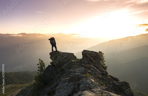 Youg man with backpack silhouette on a mauntain standing and enjoying a beautiful sunrise