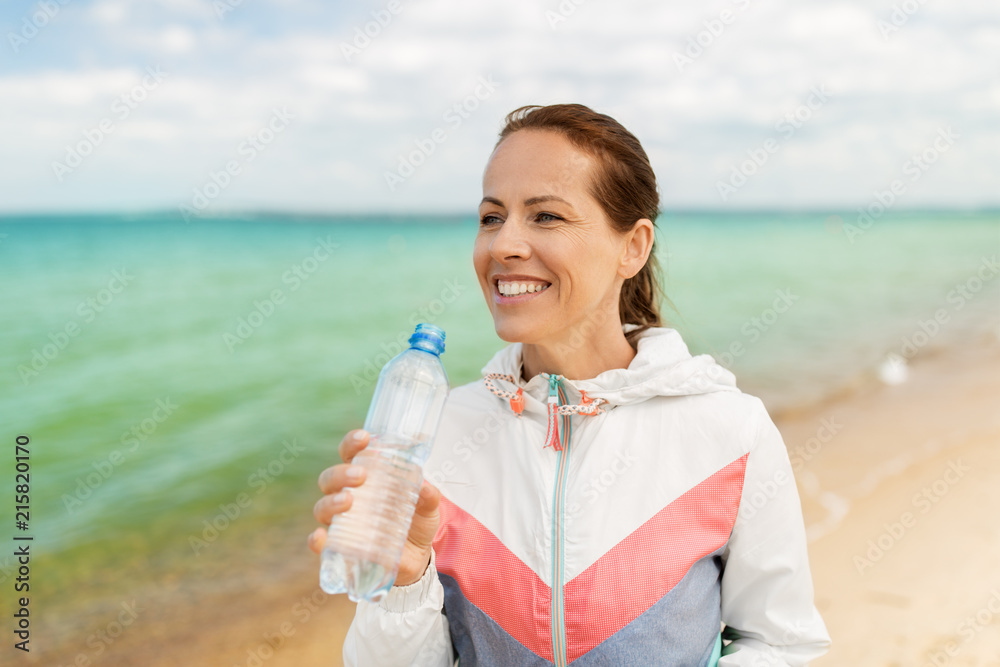 fitness, sport and healthy lifestyle concept - woman drinking water after exercising on beach fitness, sport and healthy lifestyle concept - woman drinking water after exercising on beach