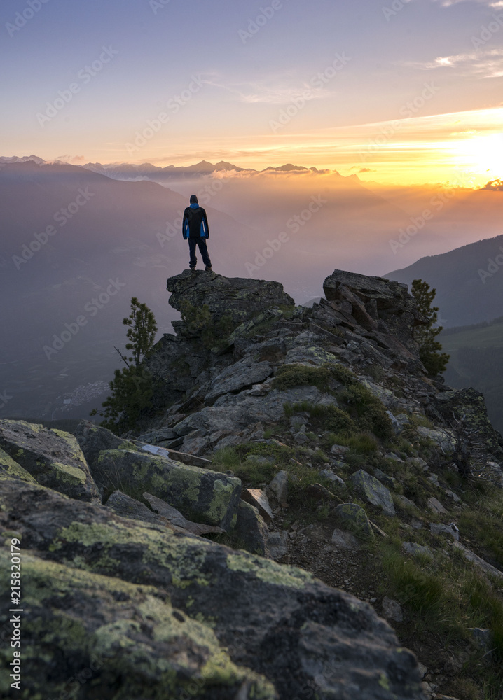 Young man standing on the Top of the mountain and enjoying total freedom during sunset in South Tyrol