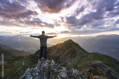 Fototapeta Naklejka Na Ścianę i Meble -  Young man standing on the Top of the mountain and enjoying total freedom during sunset in South Tyrol