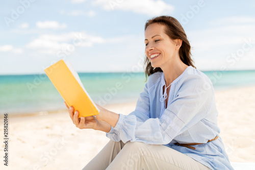 people and leisure concept - happy smiling woman reading book on summer beach