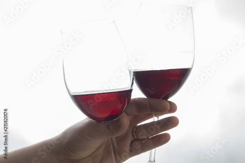 hand holding two wineglasses with red wine