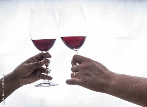 two hands holding wineglasses with red wine