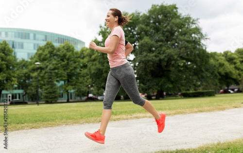fitness, sport and healthy lifestyle concept - smiling woman with earphones running at park and listening to music