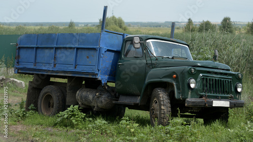 The old car is a truck. It stands in a village on the roadside with a blue body.