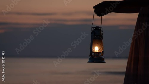 Girl in dress holding old kerosene lantern in her hand at beach after sunset at night