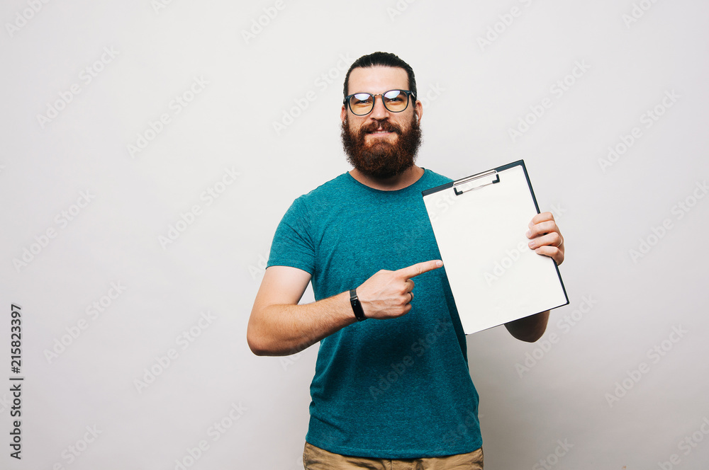 Happy bearded man wearing eyeglasses and pointing at blank white paper Happy bearded man wearing eyeglasses and pointing at blank white paper