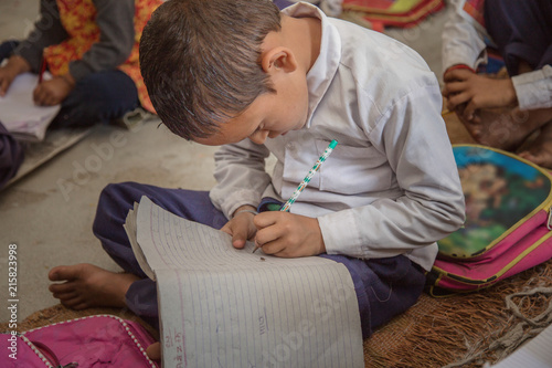 Concentrated Rural school kid studying on floor and writing in the notebook