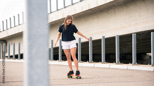 Young Beautiful Blonde Girl Riding Bright Skateboard on the Bridge
