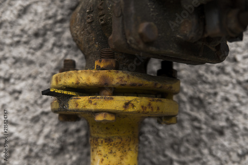 Old weathered gas crane and pipe on the background of a gray wall. Old gas gate of yellow colour is on a pipe and blocks a pipe. The pipeline with cranes for gas giving on the wall. photo