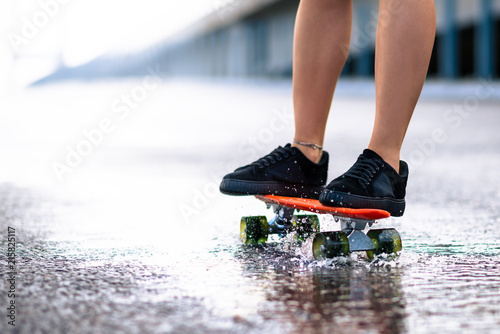 Close up of Woman Legs Riding Orange Skateboard on the Wet Road in the Rain