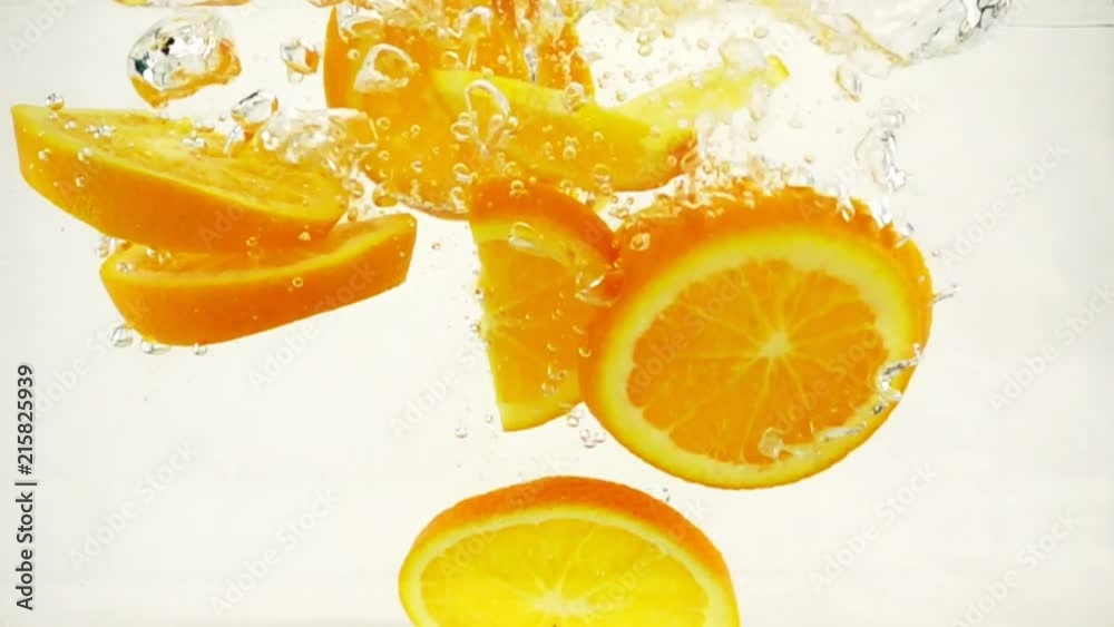 Bright juicy orange slices with a splash and bubbles falling into water, slow motion close-up