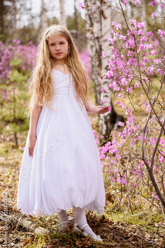 A child stands among the ledum and birch in white dress, smiling and fly hair