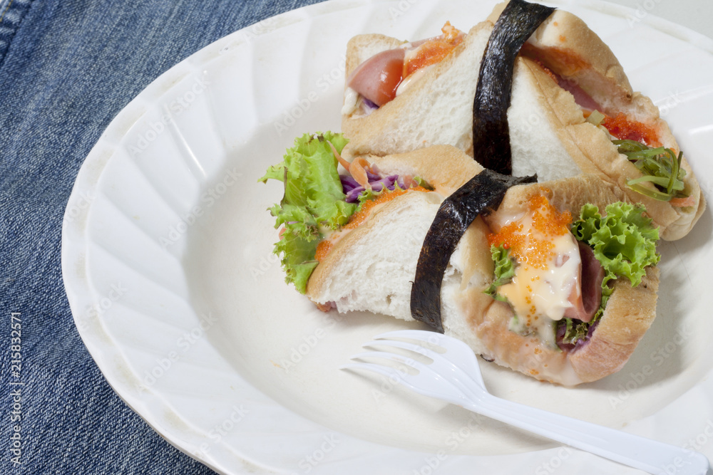 Junk food roll sandwiches with crab eggs, bacon, sliced with mayonnaise and seaweed on white plate put on the fabric. Junk food roll sandwiches with crab eggs, bacon, sliced with mayonnaise and seaweed on white plate put on the fabric.