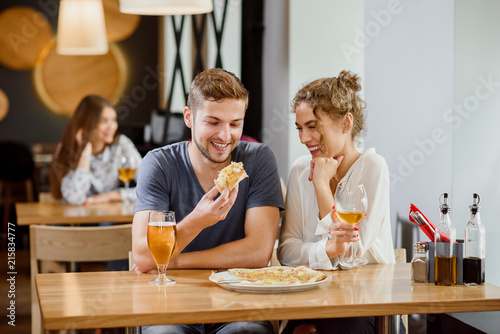 Sweet couple eating pizza and drinking beer and wine in pizzeria.