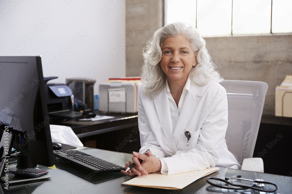 © Monkey Business - Senior female doctor sitting at desk in an office, portrait