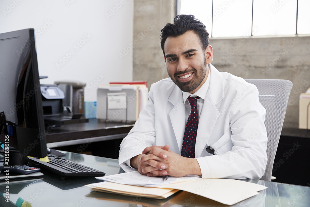 Smiling Hispanic male doctor sitting at desk, portrait