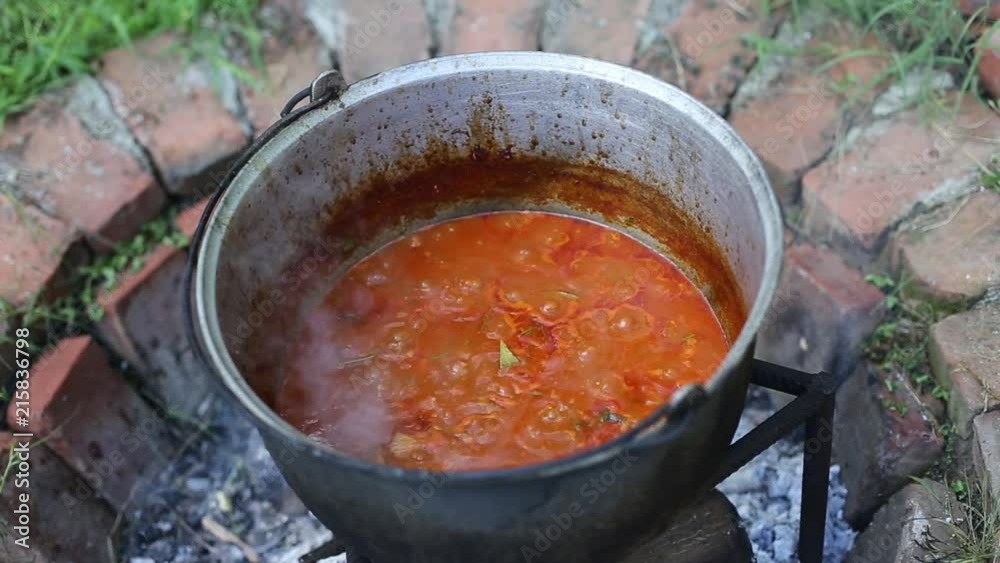 Stew cooking in an iron cast cauldron over open log fire in the backyard of a rural house Stew cooking in an iron cast cauldron over open log fire in the backyard of a rural house