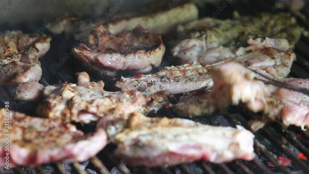 Details of a man cooking meat on a barbecue grill on a red brick fireplace in the backyard Details of a man cooking meat on a barbecue grill on a red brick fireplace in the backyard