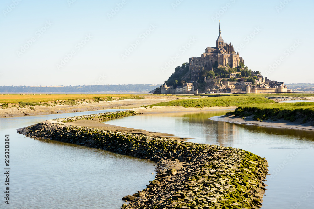 Φωτογραφία View of the Mont Saint-Michel tidal island, located in France on the limit between Normandy and Brittany, at high tide with a stone dyke on the Couesnon river in the foreground