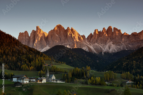 The Alpine Village of Santa Magdalena in Val di Funes with the dolomitic group of the Odle on the background during sunset in autumn season. South Tyrol, Italy. photo