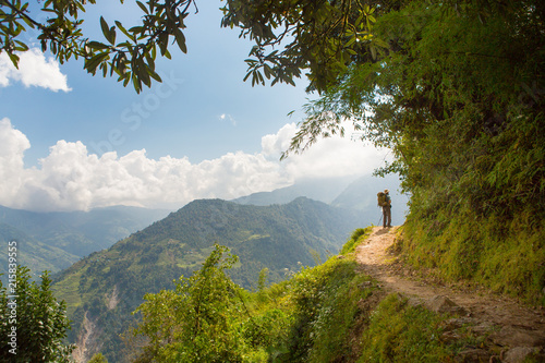 Man trekking on a trail through lush forest among terraced fields of the Himalayas in the Annapurna region of Nepal.