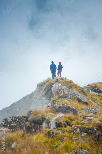 A couple standing on a ridge looking into the Annapurna moraine through the fog and clouds. Trekking the Annapurna Sanctuary to ABC in the clouds.