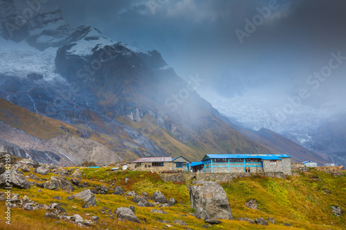 Tea house at Annapurna Base Camp at sunset with clouds surrounding the Himalayan range.