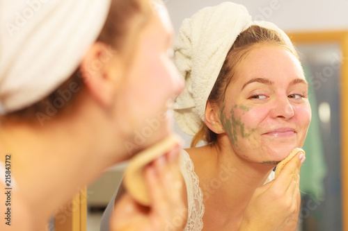 Woman removing facial clay mud mask in bathroom