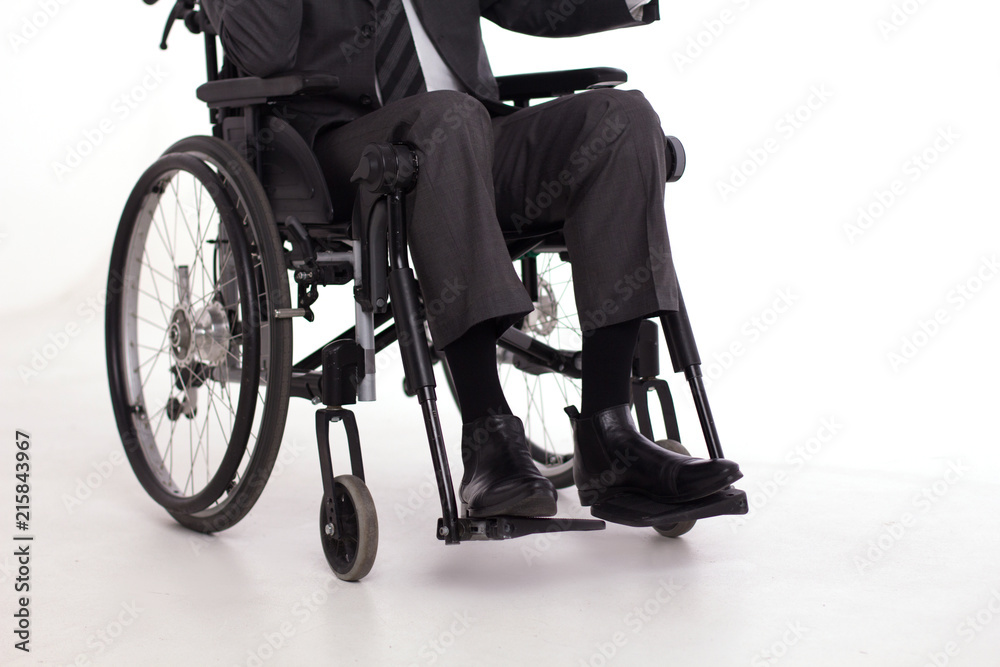 Obraz premium Mans legs in business casual pants in wheelchair. Cropped picture of man wearing formal suit and black shiny shoes sitting in wheelchair.