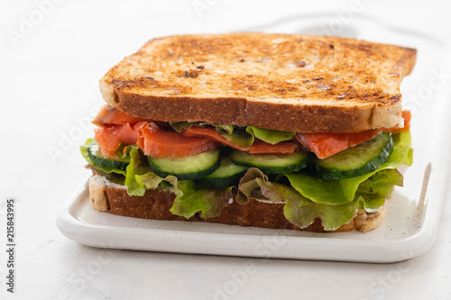 Sandwich with salmon, fresh salad and cucumber on a white board. Copy space.