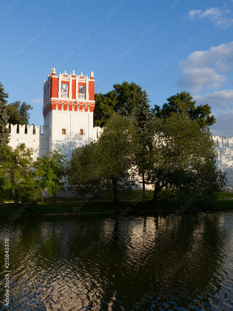 The fortress walls and towers of the Novodevichy monastery in Moscow are reflected in the water in the summer evening before sunset