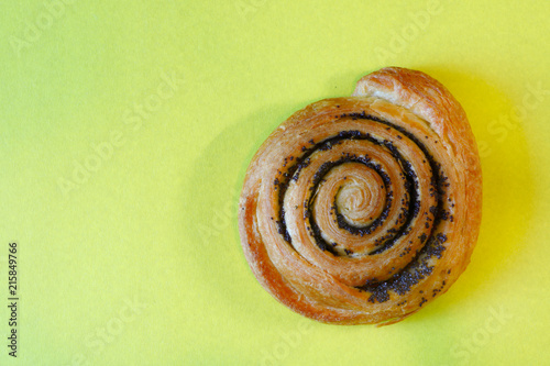delicious bun with poppy seeds in the form of a snail on yellow background